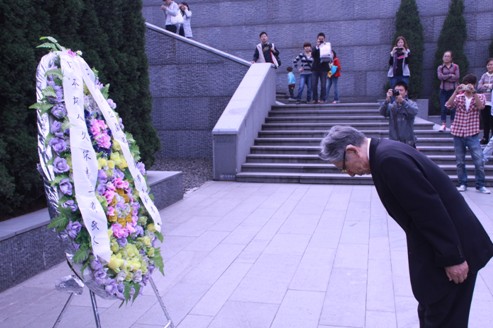 图为久保惠三郎在花圈面前为南京大屠杀遇难者鞠躬默哀